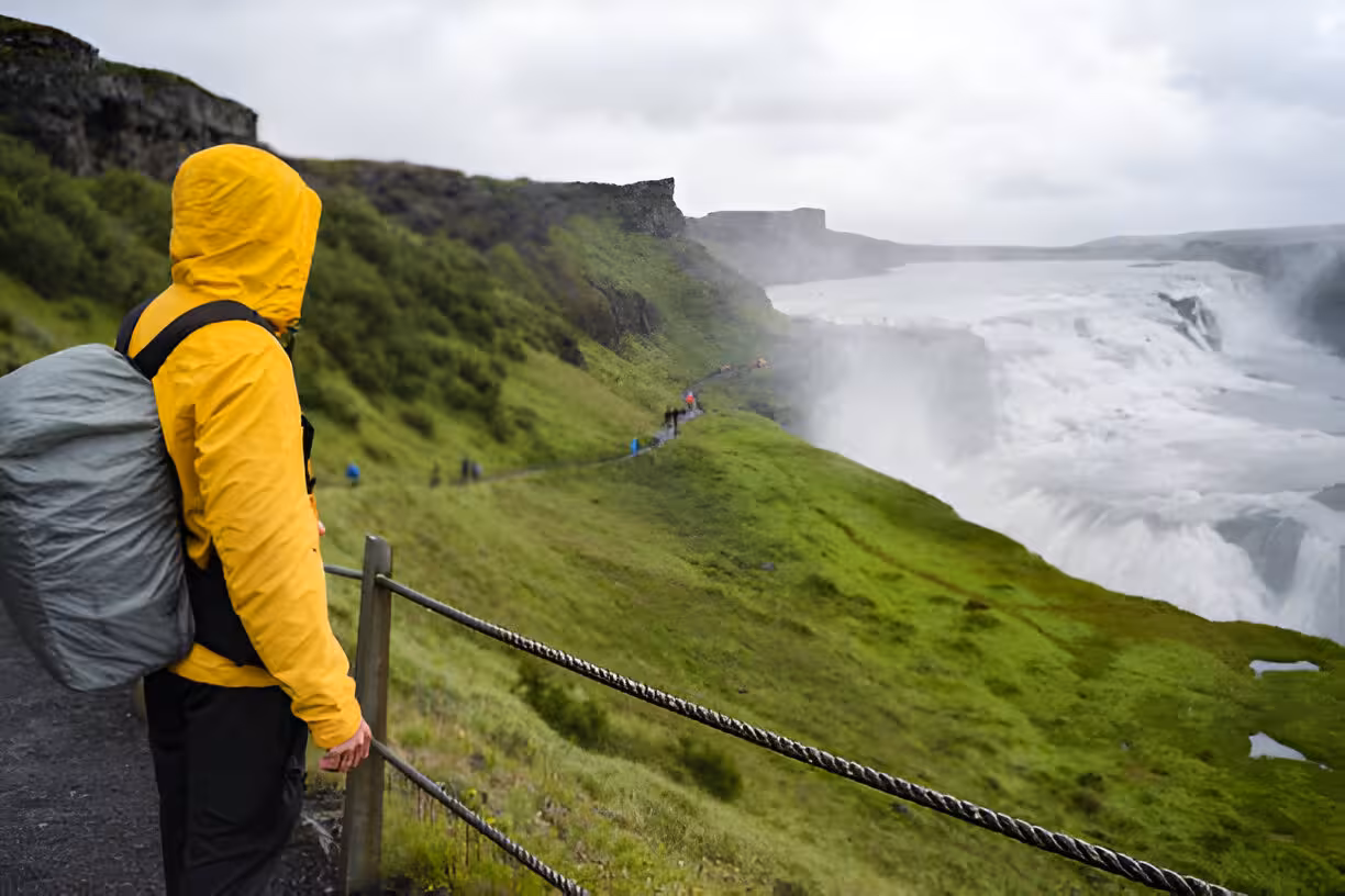 Hiker in yellow jacket with backpack overlooking Gullfoss waterfall on Iceland's Golden Circle