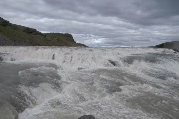 Powerful rushing waters of Gullfoss waterfall cascading over rocky tiers under cloudy Icelandic sky