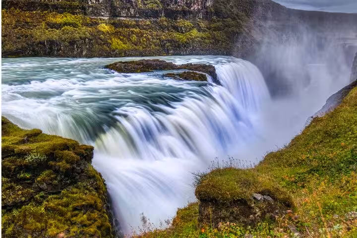 Powerful Gullfoss waterfall cascading into a misty canyon surrounded by green mossy cliffs, Iceland