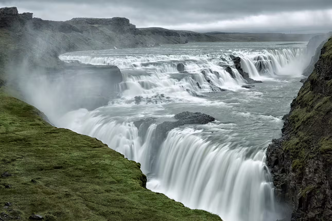 Gullfoss waterfall cascading into a canyon with misty spray and green mossy cliffs on Iceland's Golden Circle