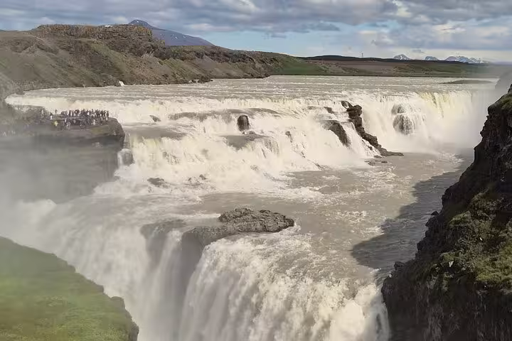 Powerful Gullfoss waterfall cascading in two tiers with mist rising, tourists visible on viewing platform, Iceland