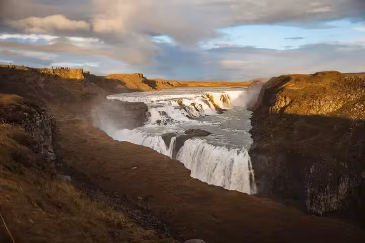 Gullfoss waterfall cascading into a canyon on Iceland's Golden Circle route under dramatic cloudy skies