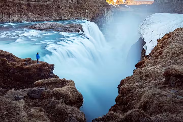 Person in blue jacket standing at edge of Gullfoss waterfall on Iceland's Golden Circle in winter