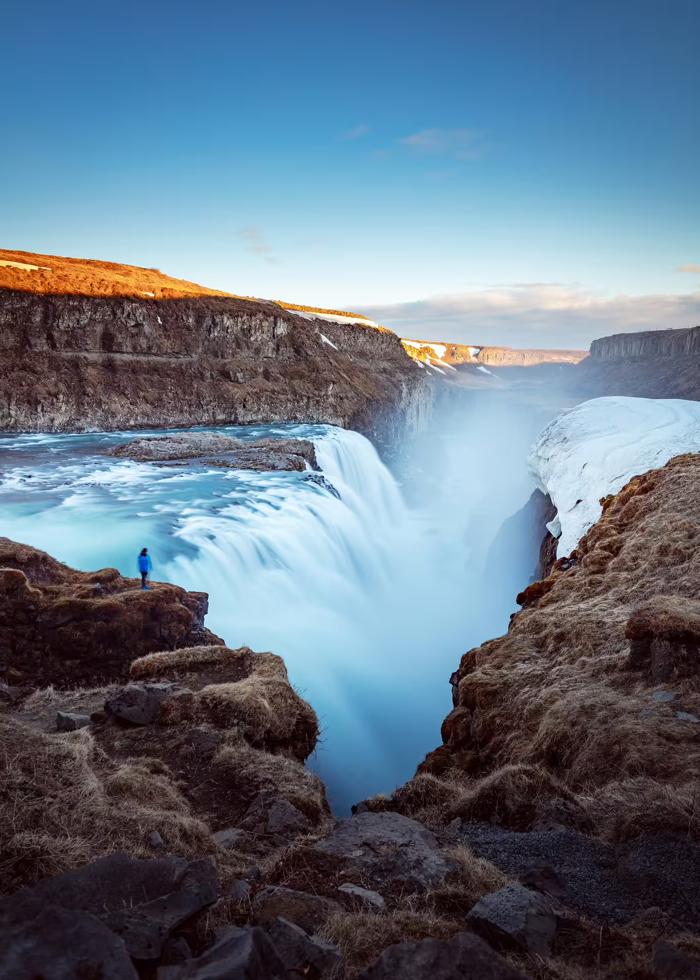 Person in blue jacket standing at the edge of Gullfoss waterfall in Iceland during winter