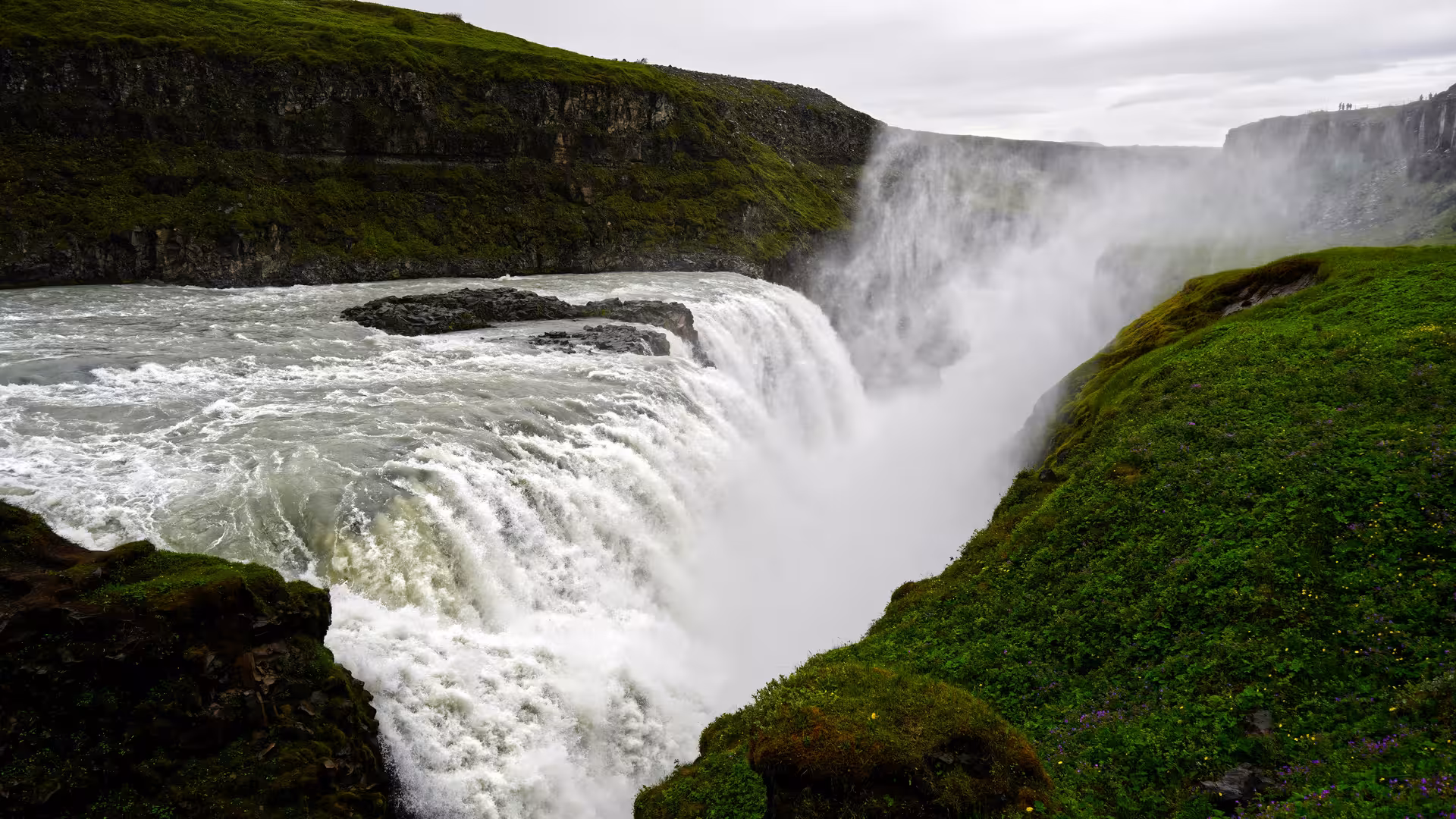 Gullfoss waterfall cascading into a misty canyon surrounded by green mossy cliffs in Iceland