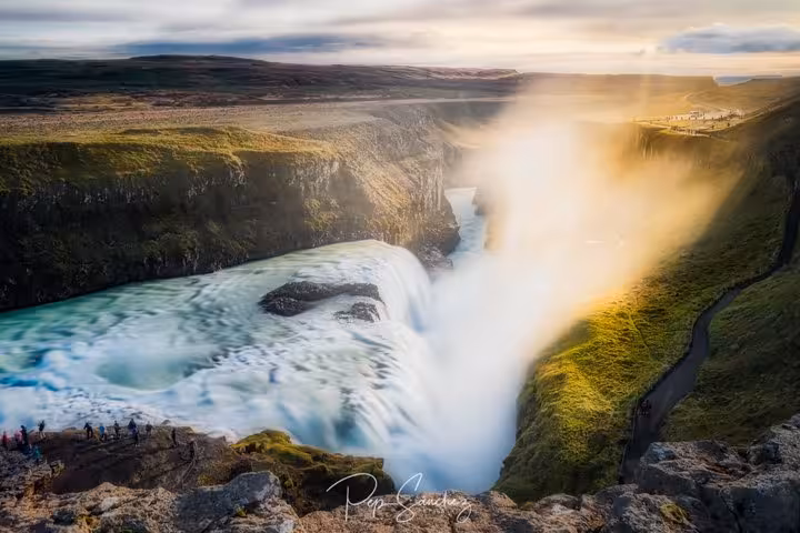 Gullfoss waterfall cascading into a canyon with golden mist and tourists viewing from rocky cliffs, Iceland