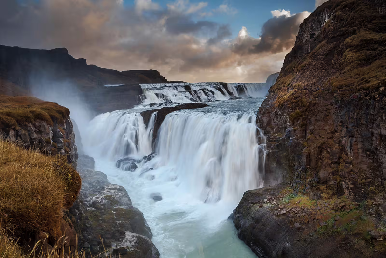 Gullfoss waterfall cascading into a canyon on Iceland's Golden Circle route under dramatic cloudy skies