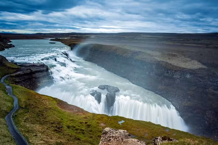 Gullfoss waterfall cascading into a canyon on Iceland's Golden Circle route under dramatic cloudy skies
