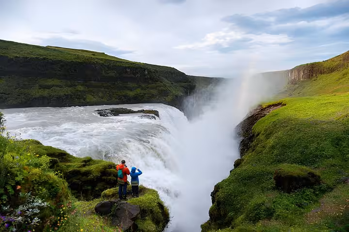 Two tourists standing on mossy cliffs overlooking Gullfoss waterfall on Iceland's Golden Circle route