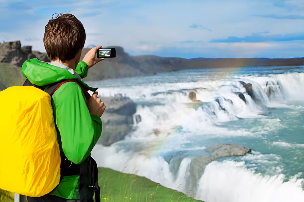 Tourist in green jacket photographing Gullfoss waterfall on Golden Circle tour from Keflavik