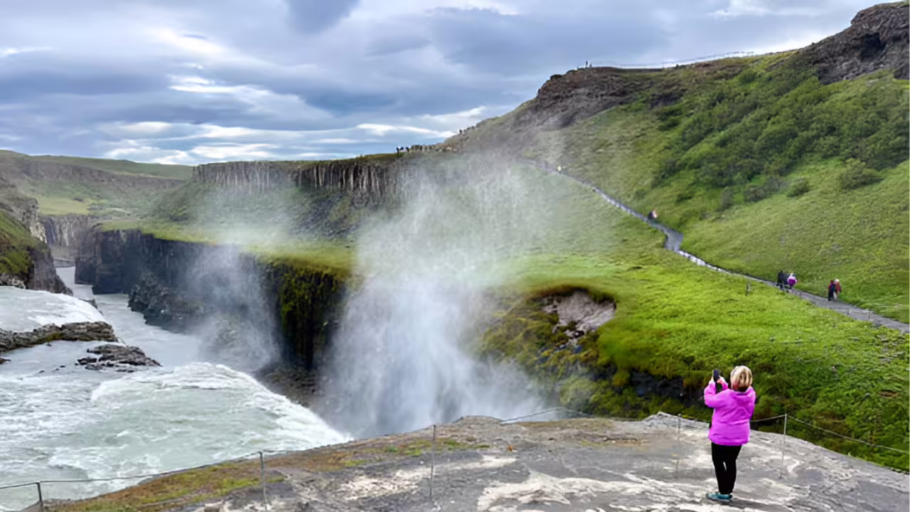 Tourist photographing Gullfoss waterfall mist rising from canyon on Golden Circle tour, Iceland