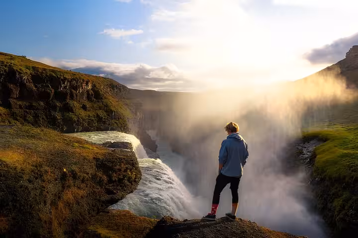 Traveler standing at edge of Gullfoss waterfall with mist and golden sunlight, Iceland Golden Circle