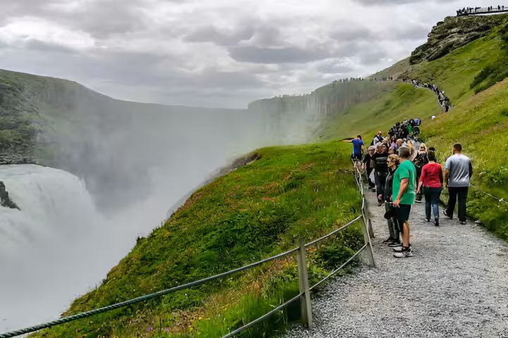 Tourists walking along a scenic gravel path beside the misty Gullfoss waterfall on Iceland's Golden Circle private tour