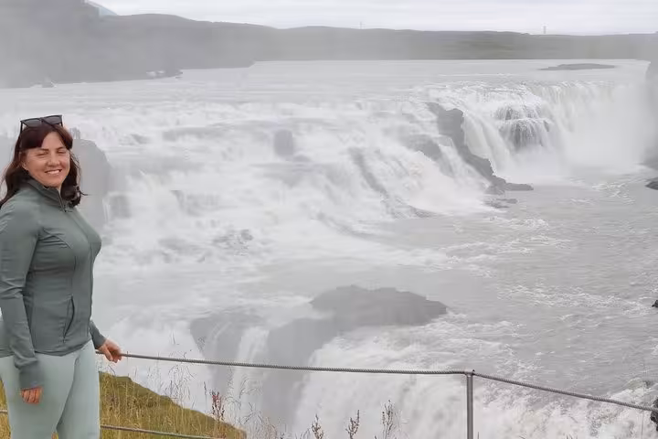 Smiling woman standing at railing overlooking powerful Gullfoss waterfall on Golden Circle tour Iceland