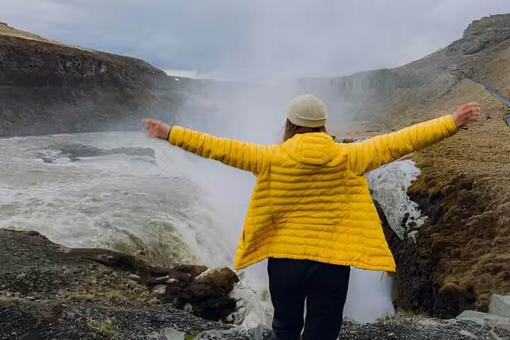 Tourist in yellow jacket spreading arms at Gullfoss waterfall on Golden Circle tour from Reykjavik