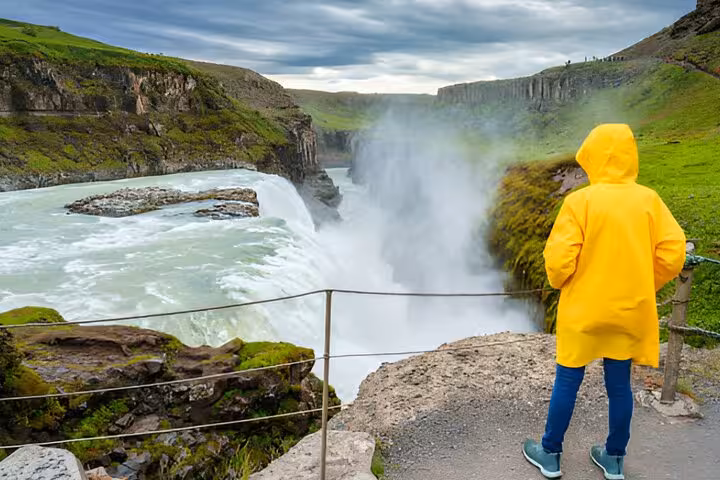 Tourist in yellow raincoat viewing Gullfoss waterfall on Golden Circle tour from Reykjavik