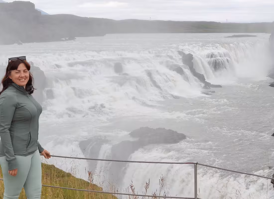 Smiling woman in green jacket standing at Gullfoss waterfall on Iceland's Golden Circle tour