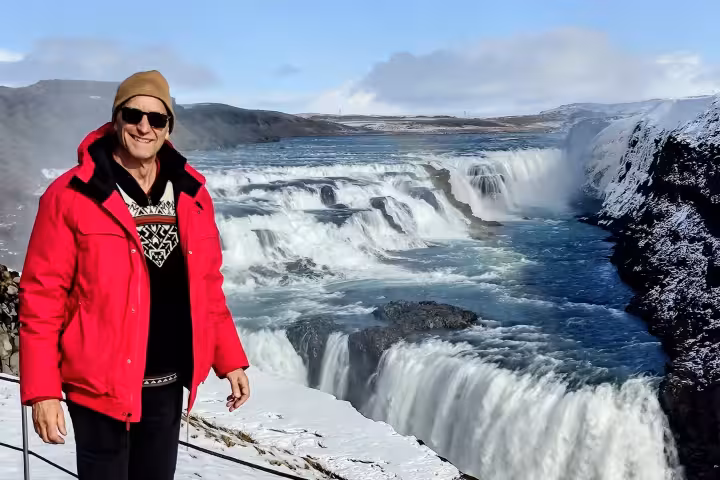 Smiling traveler in red jacket at Gullfoss waterfall with snow-covered landscape on Golden Circle tour