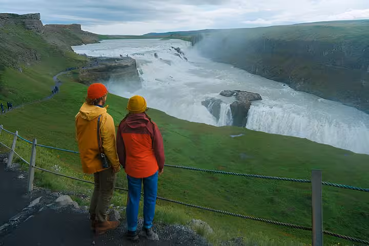 Two tourists in colorful jackets viewing Gullfoss waterfall on Golden Circle tour, Iceland