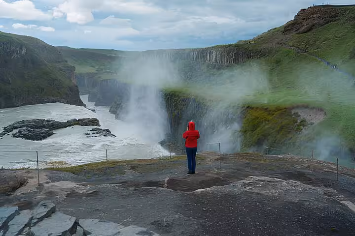 Tourist in red jacket standing at Gullfoss waterfall viewpoint on Golden Circle tour Iceland