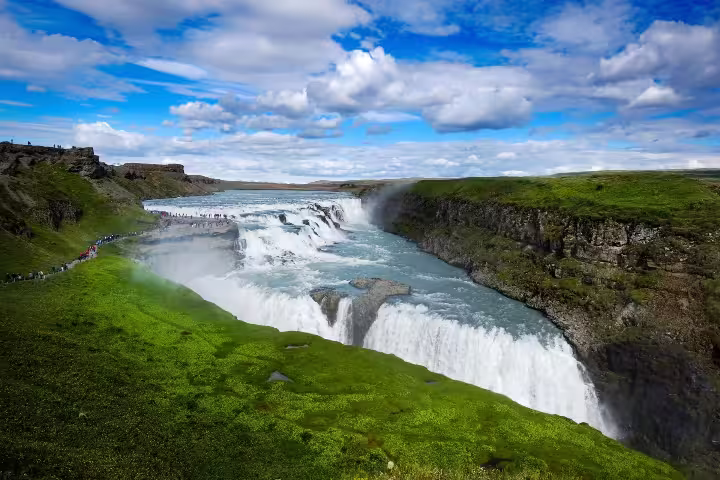 Breathtaking view of Gullfoss waterfall on a sunny day, surrounded by lush greenery, part of the Golden Circle Adventure tour.