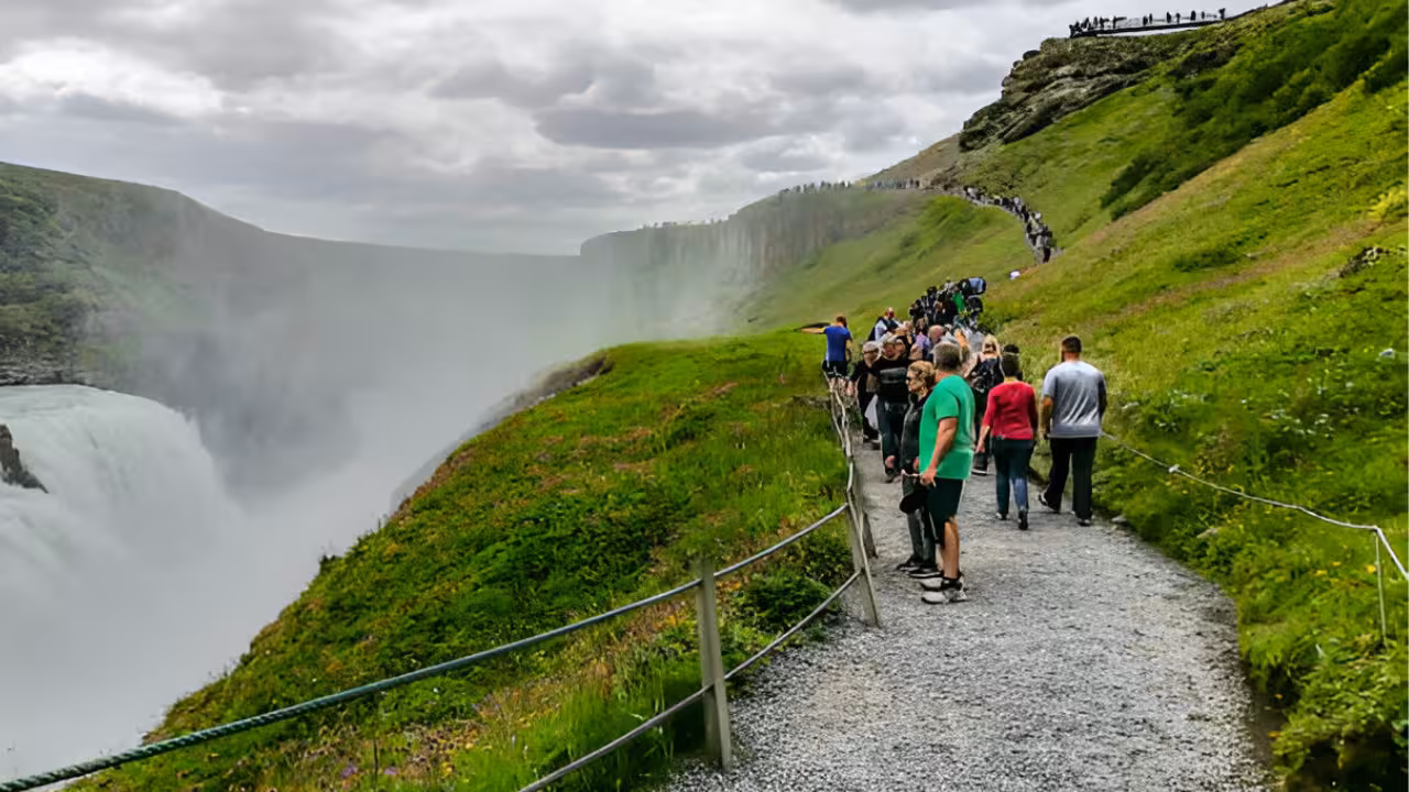 Tourists walking along a scenic gravel path beside Gullfoss waterfall on Iceland's Golden Circle route