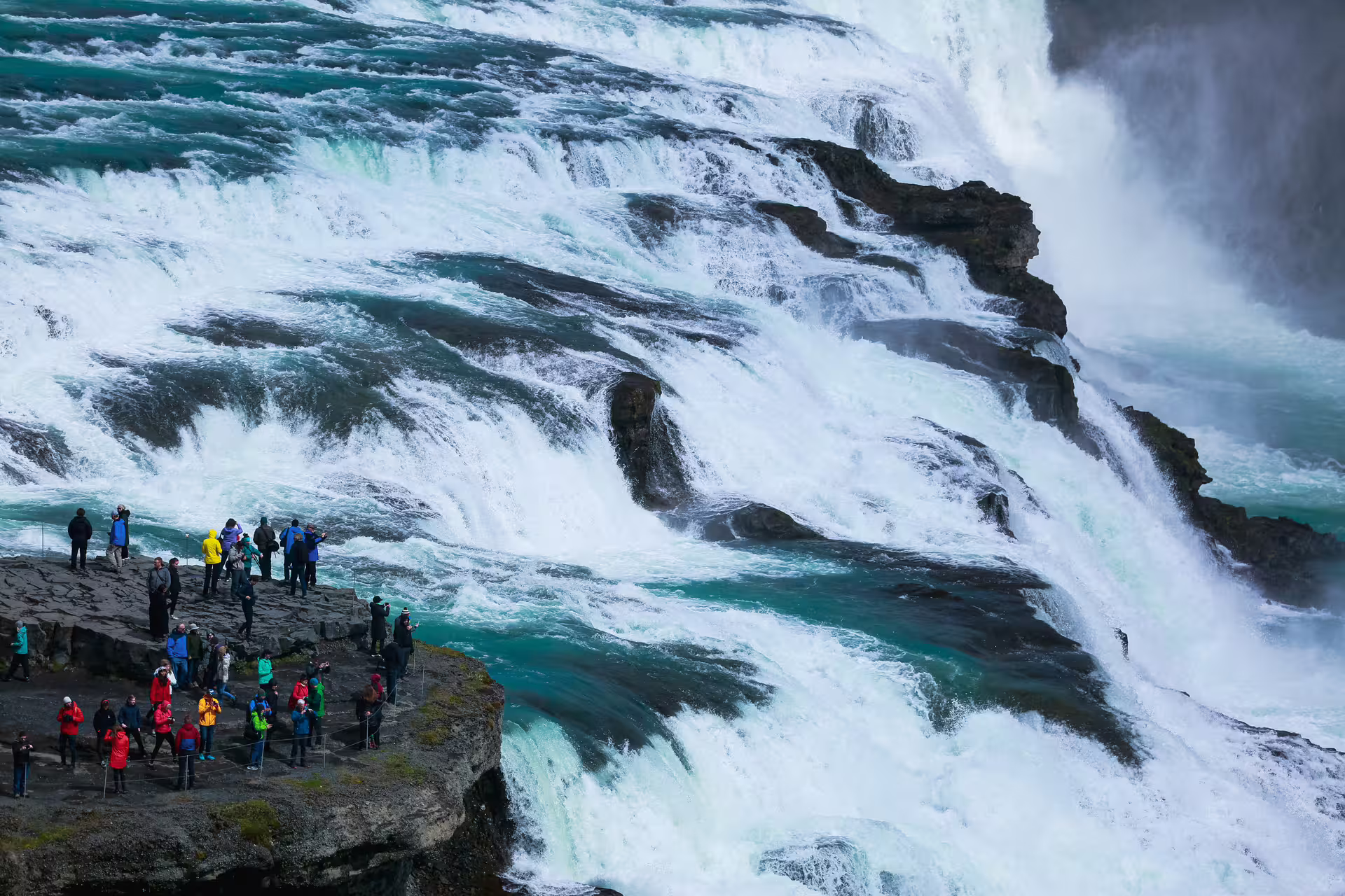Tourists on rocky viewpoint overlooking powerful cascading waterfalls of Gullfoss on Iceland's Golden Circle