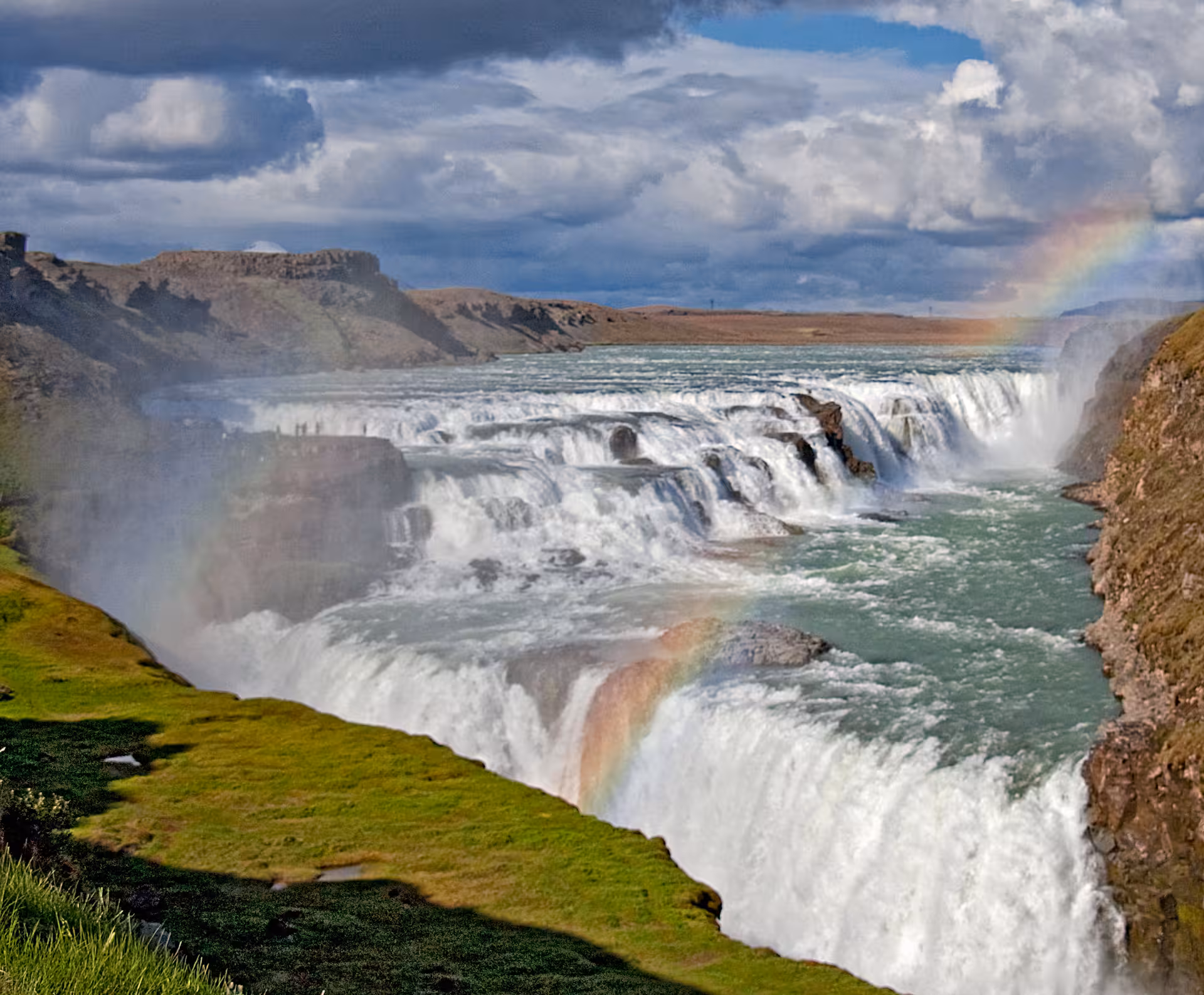 Gullfoss waterfall on Iceland Golden Circle tour, cascading into canyon with rainbow and dramatic skies