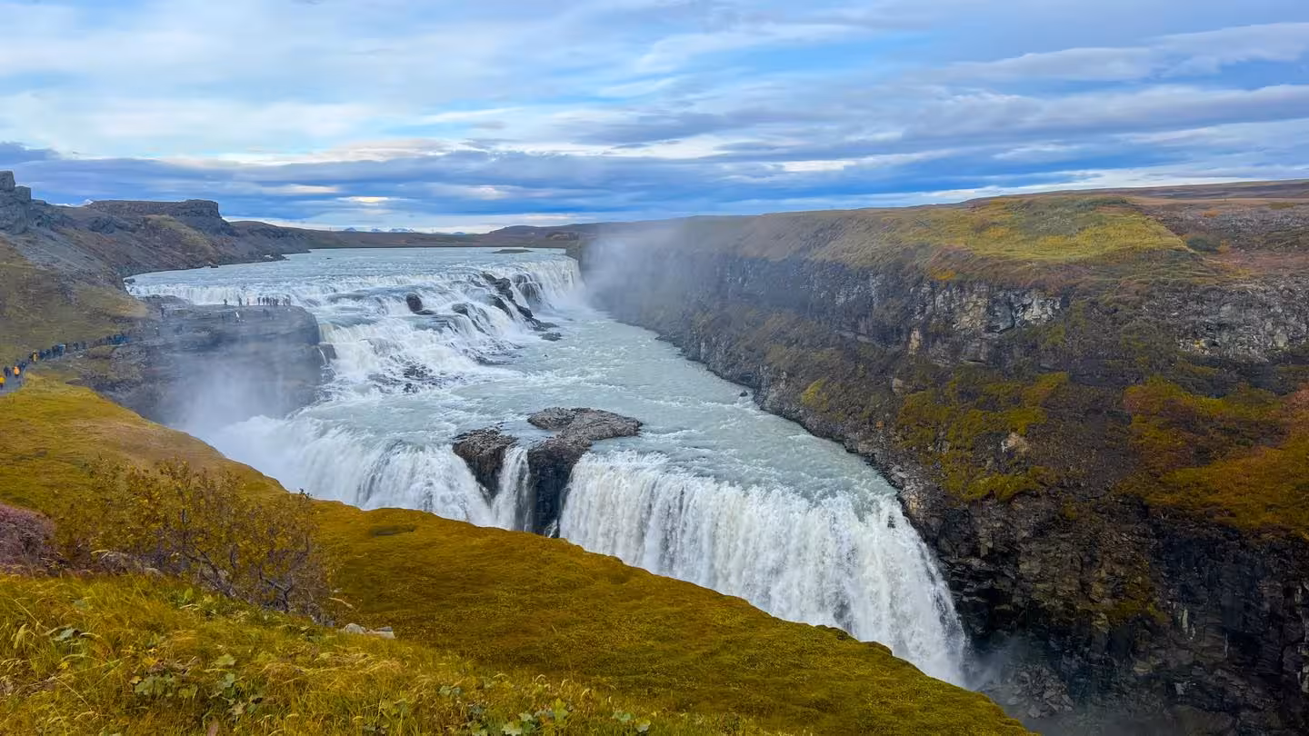 Gullfoss waterfall cascading into a canyon with misty spray and green hillsides in Iceland