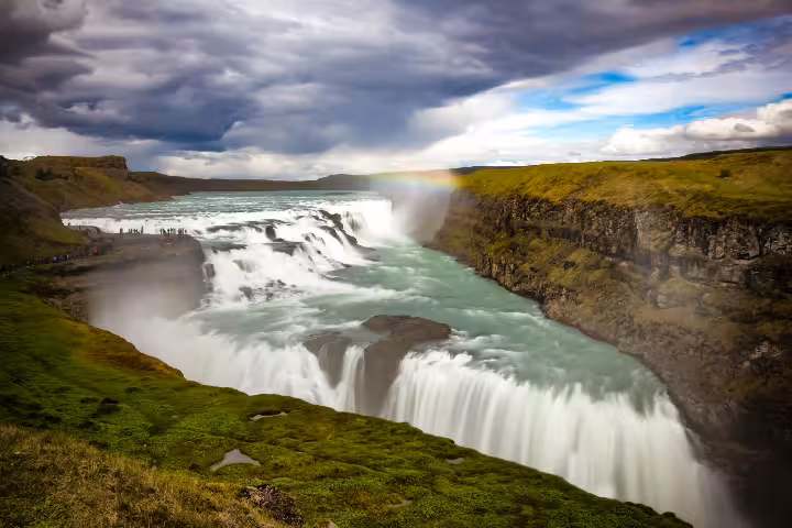 Gullfoss waterfall cascading into a canyon with a rainbow and dramatic skies on Iceland's Golden Circle
