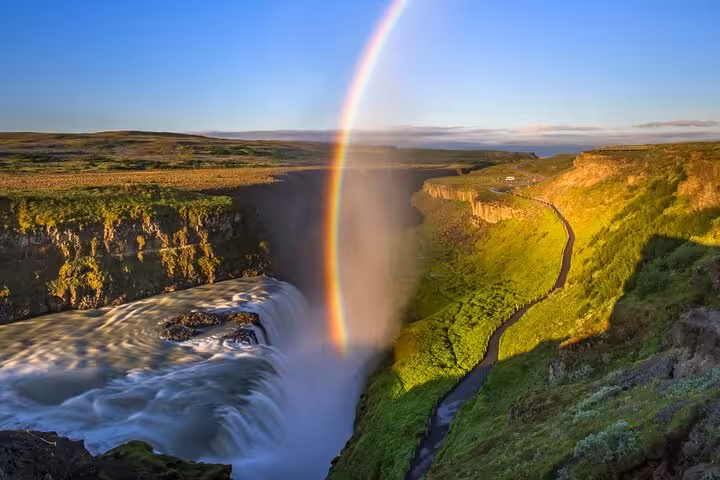 Rainbow over Gullfoss waterfall cascade into dramatic canyon with lush green cliffs, Iceland Golden Circle