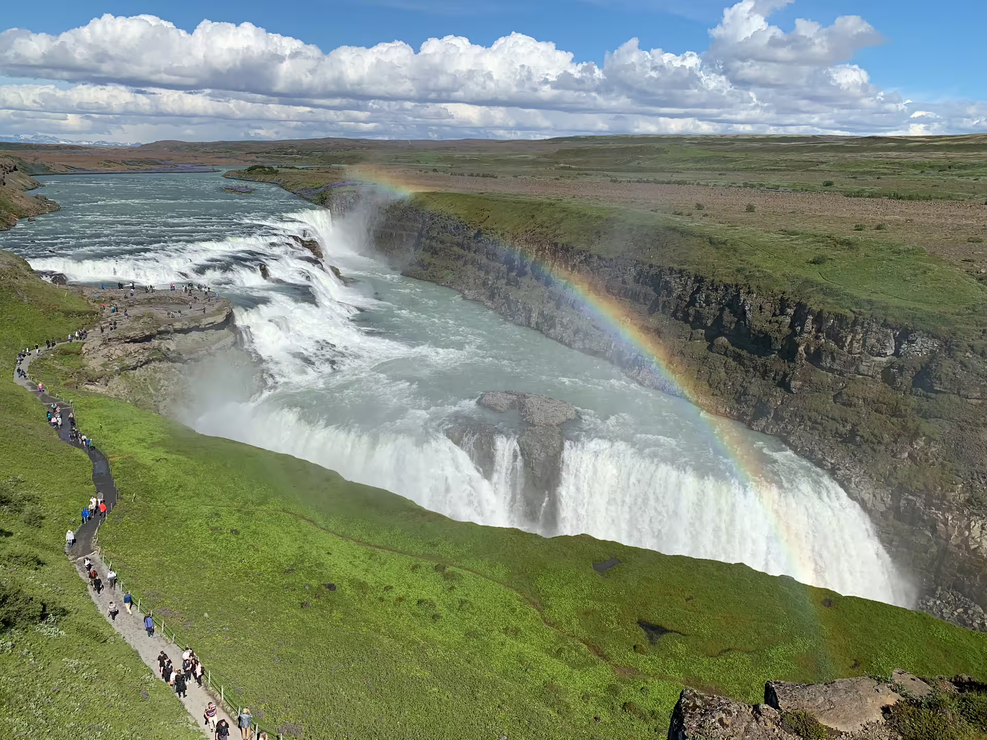 Gullfoss waterfall with rainbow on Iceland's Golden Circle, tourists on viewing path beside cascading falls