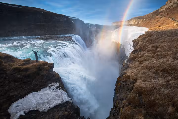 Person with raised arms at Gullfoss waterfall with rainbow on Iceland's Golden Circle route