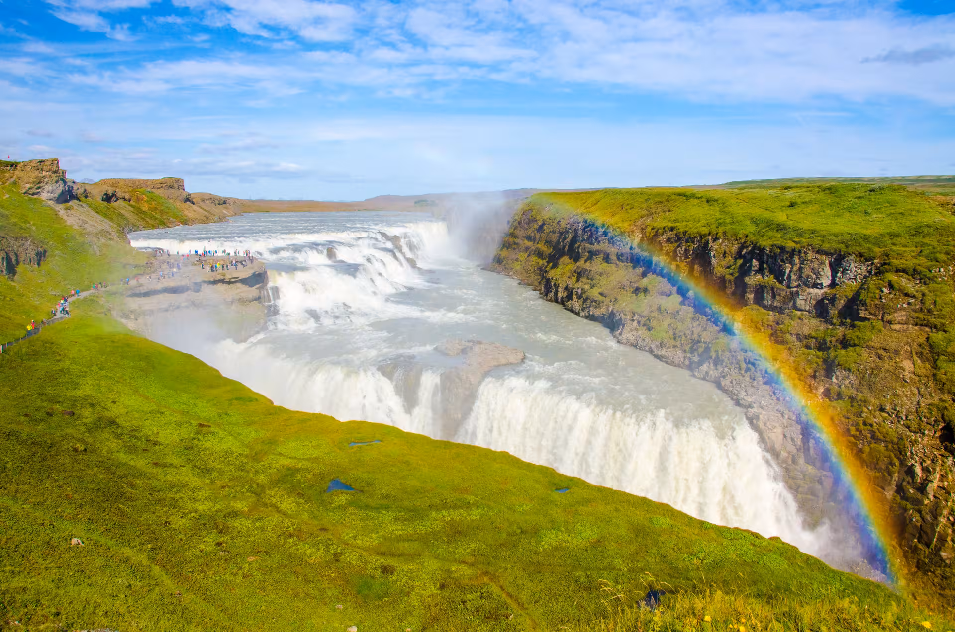 Stunning view of Gullfoss waterfall with a vibrant rainbow in Iceland's scenic landscape on a sunny day.