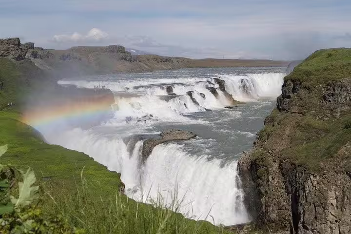 Gullfoss waterfall in Iceland with a rainbow rising from the mist, surrounded by green cliffs