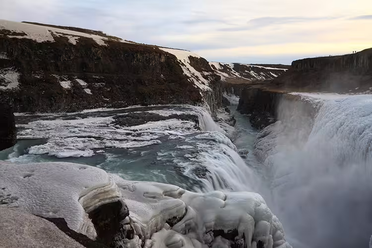 Gullfoss waterfall in winter with ice-covered rocks and turquoise water flowing through a canyon, Iceland
