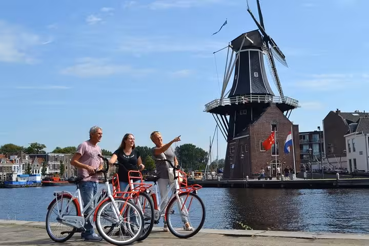 Guided Haarlem bike tour group with Dutch bikes by the river, viewing the De Adriaan windmill and waterfront
