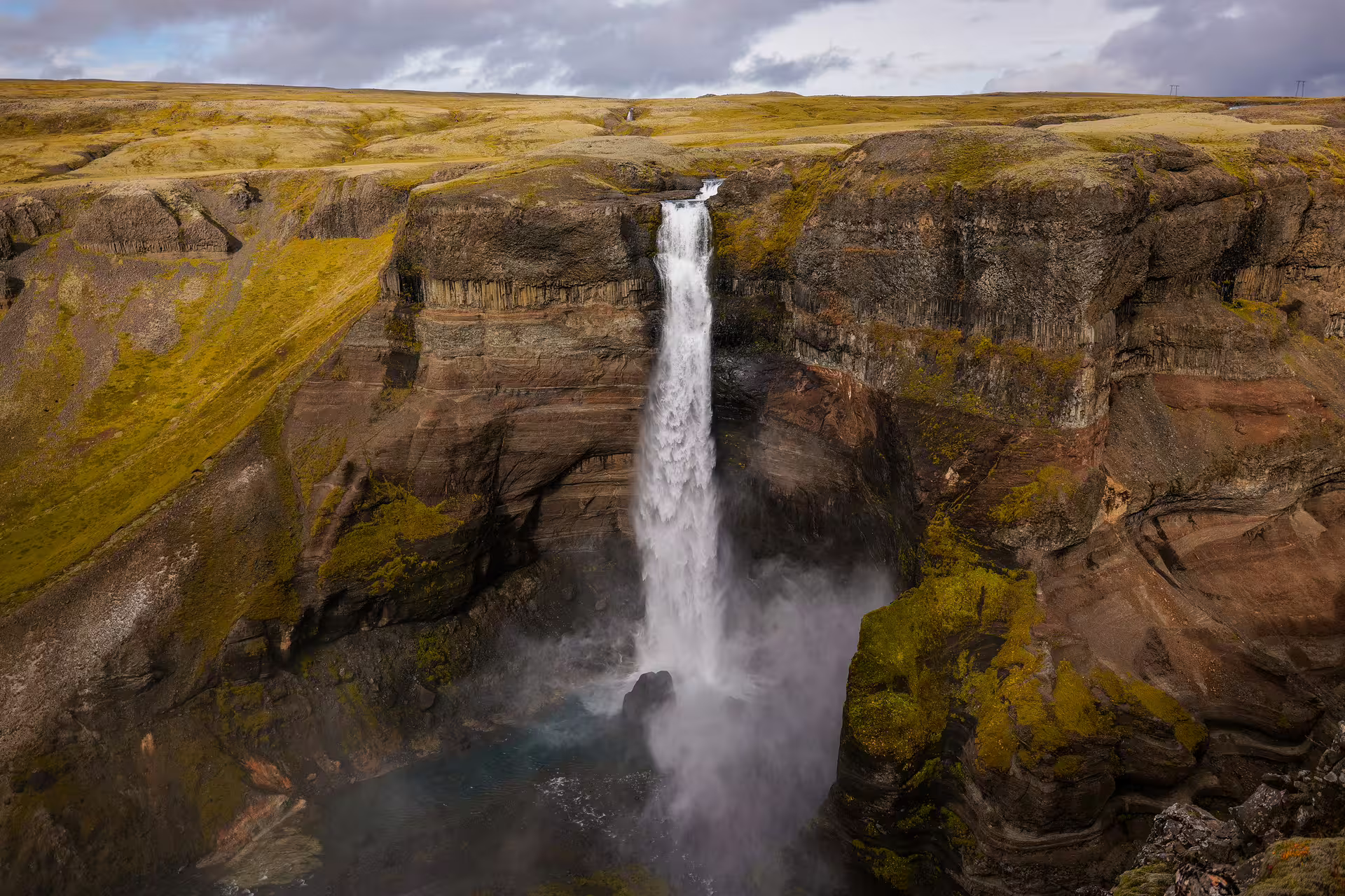 Dramatic Haifoss waterfall plunging into a misty gorge surrounded by mossy basalt cliffs in Iceland highlands tour