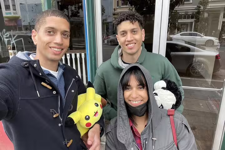 Three friends smiling on Haight-Ashbury street holding Pikachu plush toy in San Francisco