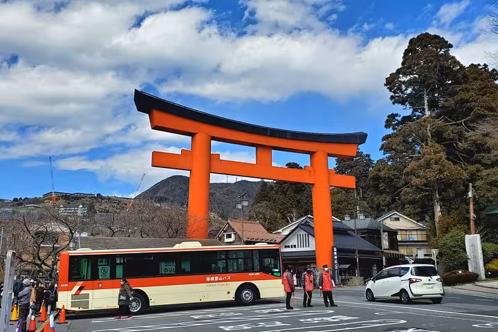 Iconic red torii gate at Hakone Shrine with a tour bus and mountain backdrop on a 2-day Tokyo Mt Fuji Hakone guided tour