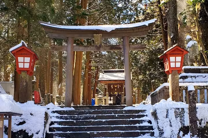 Snow-covered stone steps leading to a wooden torii gate flanked by red lanterns at a serene Hakone shrine in winter