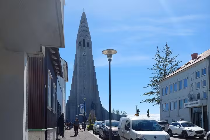 Hallgrímskirkja church tower rising above Reykjavik street with parked cars and pedestrians on sunny day