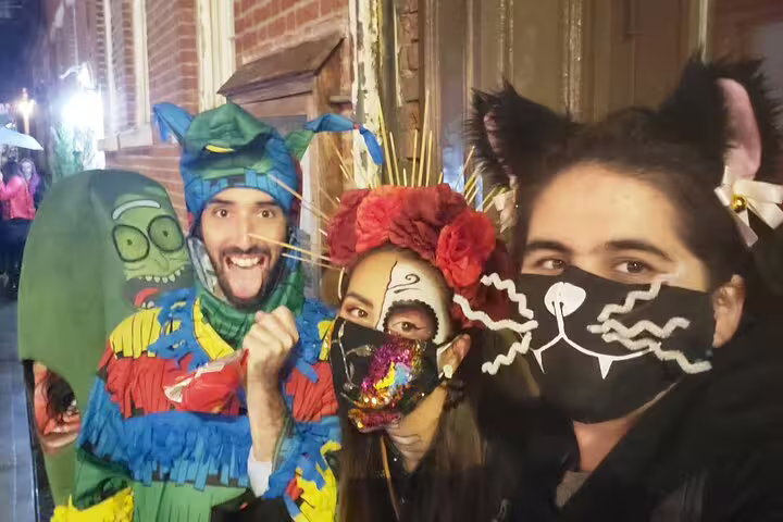 Group of four people in colorful Halloween costumes and masks on a nighttime city street tour