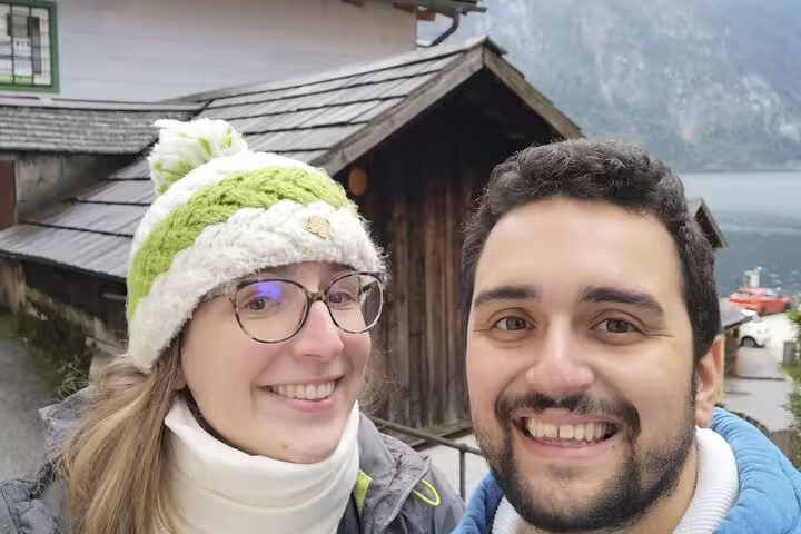 Smiling couple taking selfie during Hallstatt outdoor escape game tour with alpine lake and wooden buildings behind