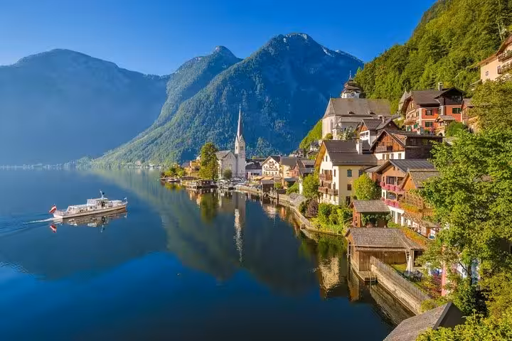 Sunny Hallstatt lakeside panorama with church spire and boat, classic view on small-group day trip from Vienna