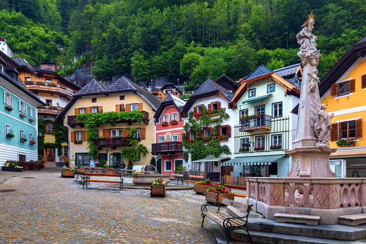 Colorful historic buildings and baroque fountain in Hallstatt town square with lush green hills behind