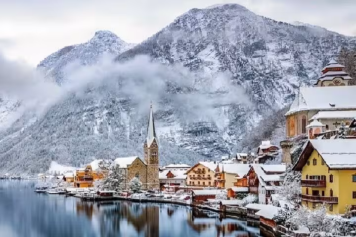 Snowy Hallstatt waterfront with church spire and Alps, winter highlight on Salzburg and Hallstatt private day tour
