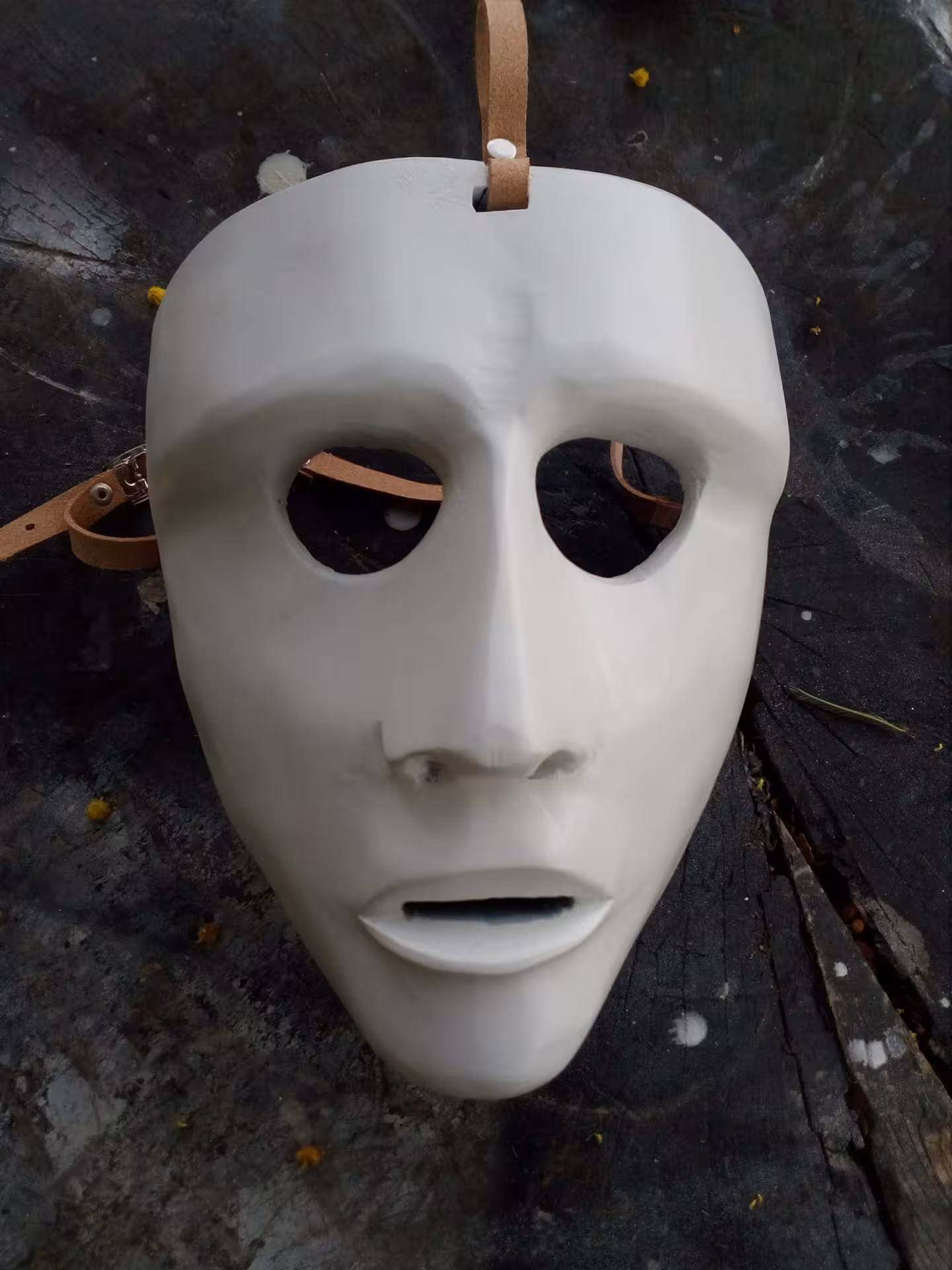 Close-up of a handcrafted white Sardinian mask with leather straps on a rustic surface.