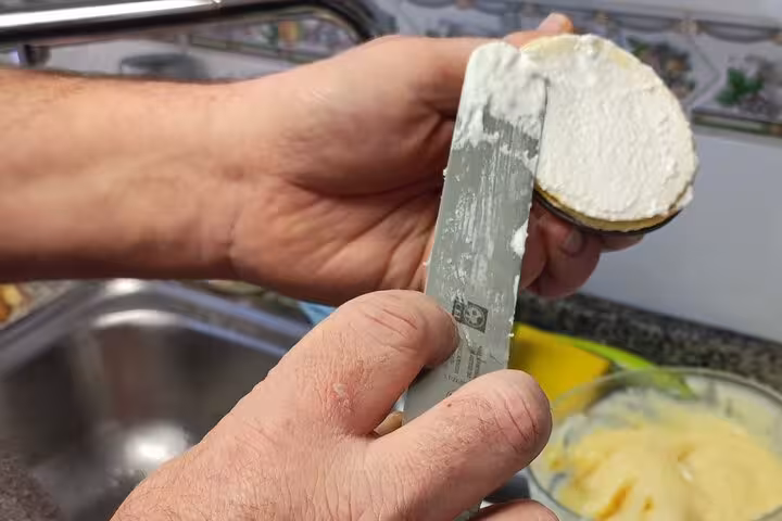 Hands spreading creamy filling onto pastry shell, preparing traditional pastel de nata, a Portuguese favorite.