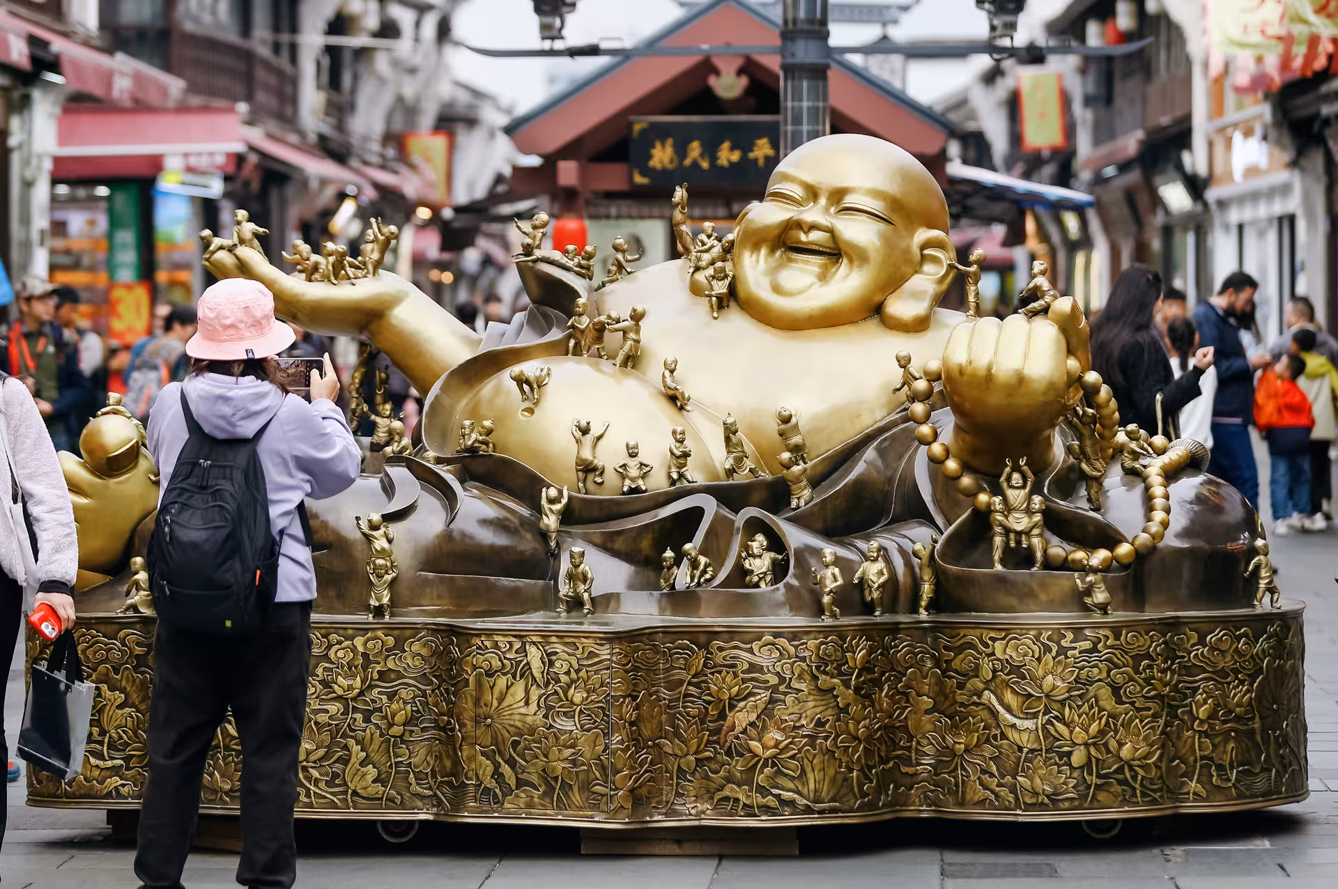 Tourists admire a large golden Buddha statue on bustling Hefang Street, highlighting Hangzhou's cultural allure.